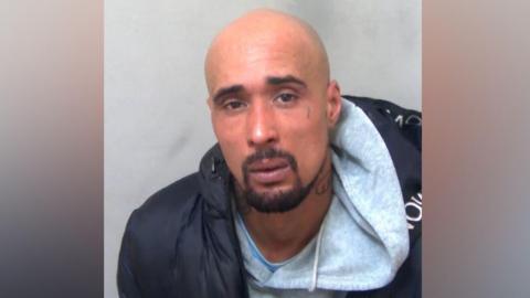 Ashley Warren in his custody photo, wearing a grey hoodie and black coat.