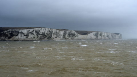 The white cliffs of Dover behind a stormy sea. The sky looks dark.