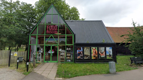 Exterior of the Food Museum showing a glass fronted triangular building surrounded by fencing and grass