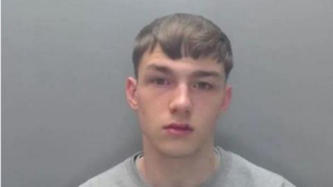 A mugshot of Jack Lawson. He has brown hair and a split upper lip. He is wearing a grey jumper.