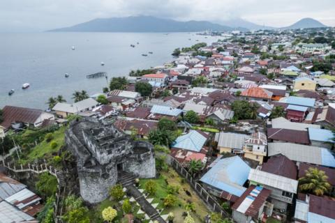 Rows of houses with corrugated iron roofs line the seafront with an old grey fortification in the foreground