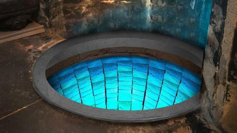 A well set into stone in a cathedral - its walls are lined with turquoise blue mosaic tiles and it is lit in soft blue light.