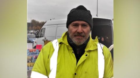 Francesco Galia is pictured wearing a black hat, black jumper and a hi-vis jacket. He has a grey moustache and beard. 