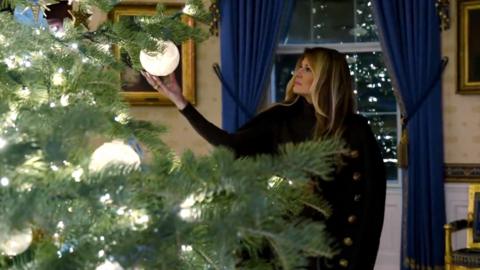Melania Trump is touching a decoration from the Christmas tree.