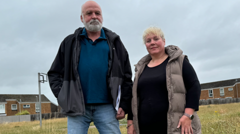 Garth Tolmie and Jane Seaney standing on grassy land with houses behind them