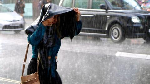 A woman holds her jacket over her head as rain pours down in London