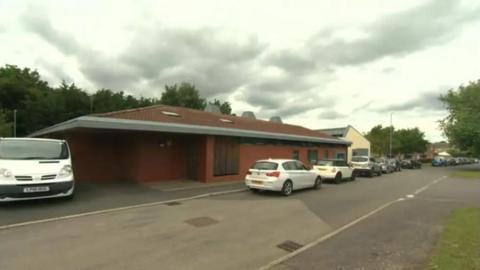 Exterior of a brick building with several cars parked on the road in a line next to the entrance of the children's home
