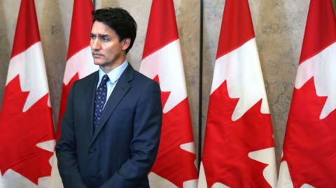 Justin Trudeau standing before Canadian flags 