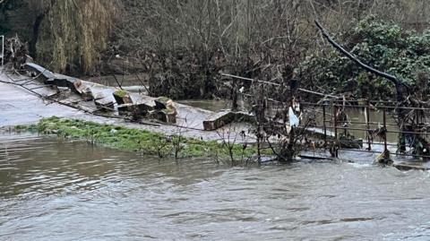 A flooded Pack Bridge in Bradford-on-Avon, with loose debris to one side.