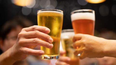 Two people cheers two pints glasses full of beer and cider.