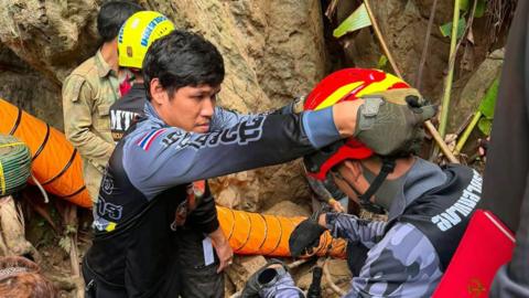 A handout photo made available by Metta Tham Kalasin Rescue shows Thai rescuers on a mission to free seven Laotians trapped in a flooded cave in Xaysomboun province, Laos, 25 May 2026. A rescuer places a protective helmet on the head of another rescuer