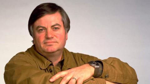 Roger Cook wearing a brown shirt in a studio shot.