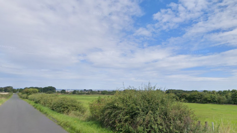 A green field site with a rural road alongside 