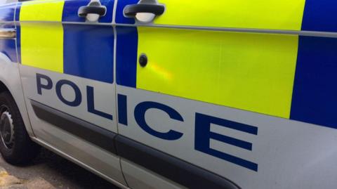 Side of a white police van with blue and yellow thick stripes on the side, with POLICE below.