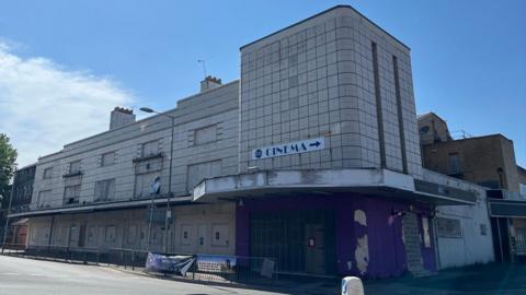 An old cinema building is pictured by a road.
