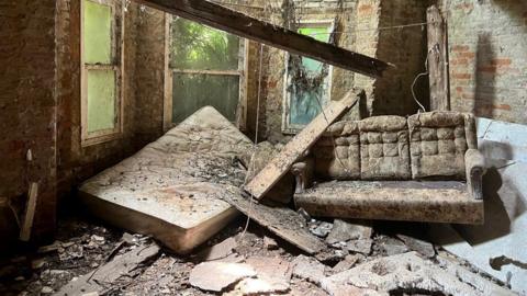 A dilapidated home with a sofa and mattress covered in debris.