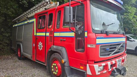 A red Volvo fire engine with a fire hose and branches, before it is due to be transported to Malawi