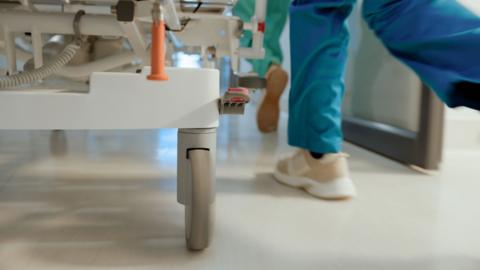 Doctors feet running through hospital corridor next to wheels of hospital bed