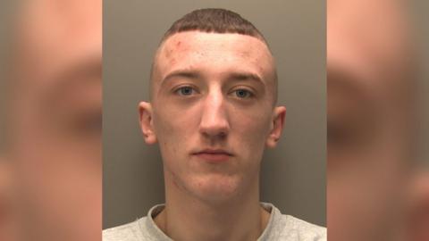 A police-issued custody image of a man with cropped brown hair wearing a grey sweatshirt