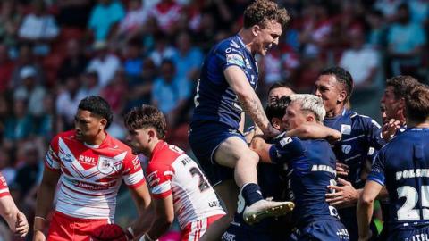 Toulouse players, in dark blue, celebrate a try against St Helens, two of whose players, in red and white, look disconsolate.