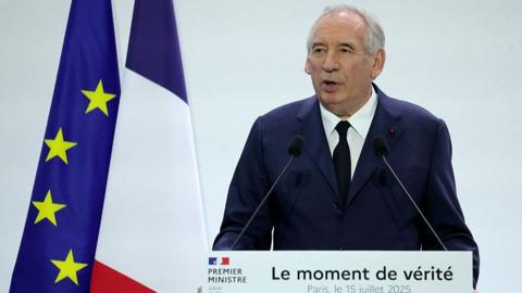 Francois Bayrou stands in front of a lectern reading "The moment of truth". Behind him are a French and an EU flag