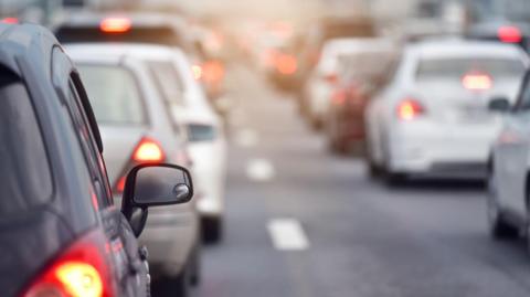 A number of cars stuck in traffic along a road with white lines down the middle.