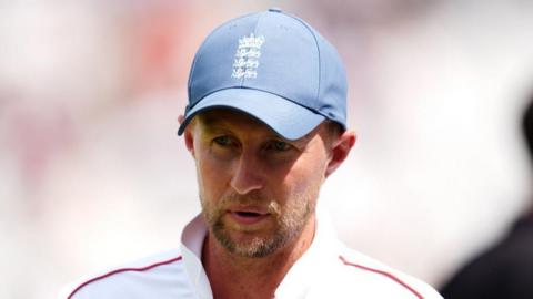 Joe Root wears a White cricket top and blue cap.