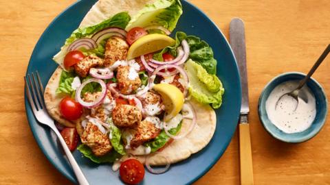 Microwave spicy chicken pitta — It's chicken bites on lettuce, cherry tomatoes, lemon, red onion and a pitta. It's all sitting on a blue plate. It looks colourful and appetising, accompanied by a small pot of mayonnaise in a ramekin that matched the plate.