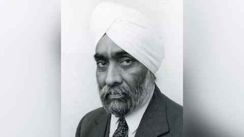 Black-and-white undated portrait image of Gyani Sundar Singh Sagar, also known as Gyani Ji. He has a beard and is wearing a turban as well as a dark suit and tie and white shirt.