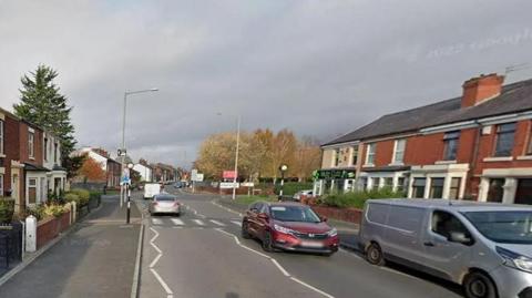 Vehicles driving on Station Road showing a pelican crossing 