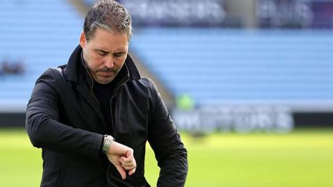 Marti Cifuentes looks down at his watch while preparing for a game as Leicester City manager