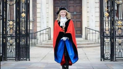 Worcester mayor Mel Allcott dressed in her official robes and chain of office standing with arms folded in front of her and next to the ornate black gates of the Guildhall