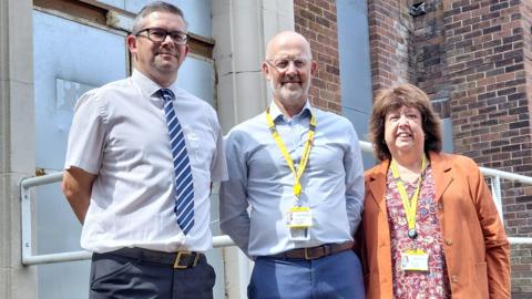 Andrew Chandler from Cheshire Leisure (left) with Mick Warren (centre) and Dawn Clark (right) from Cheshire East Council. They are standing in front of the closed swimming baths, with a door boarded up with a metal sheet