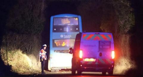 A blue Translink bus stopped on a country road with one emergency worker on standby