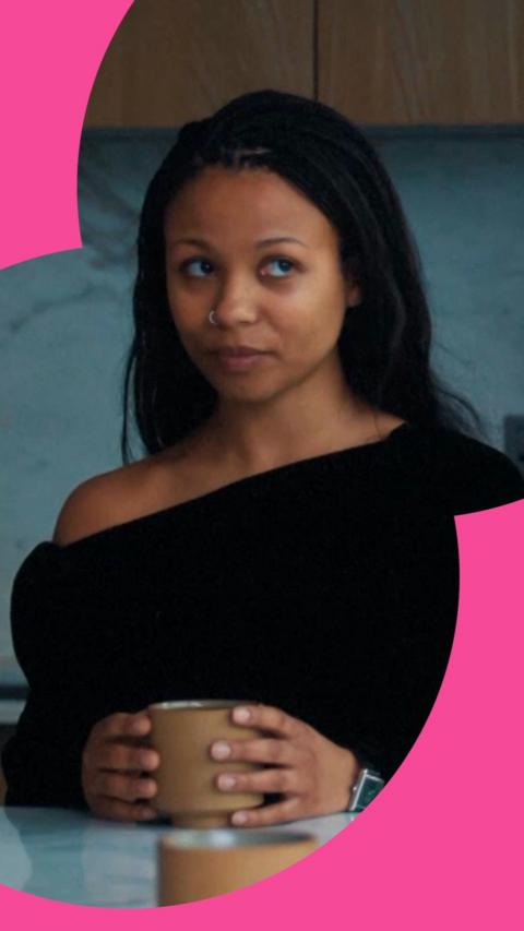 Industry character Harper looks to the side while holding a mug on a table. She has long black hair and wears a black top