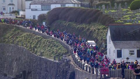 Hundreds of competitors running along a clifftop road