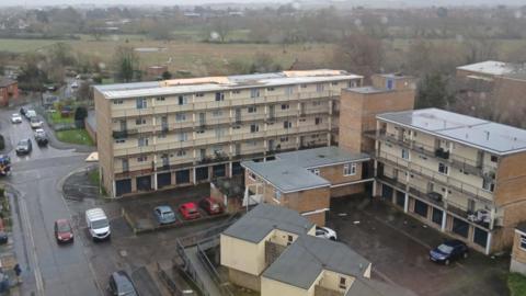 A picture of the block of flats at Westfield Close with parts of the roof missing.  The picture was taken during Storm Darragh and shows a cloudy, rainy day.