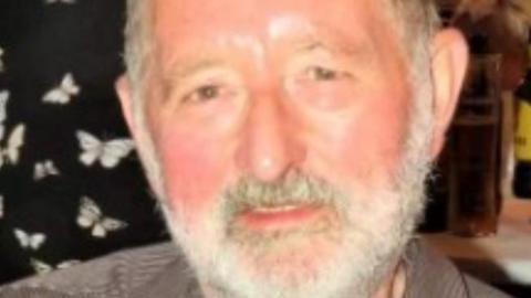 A bearded man smiling at the camera. His facial hair is white. 