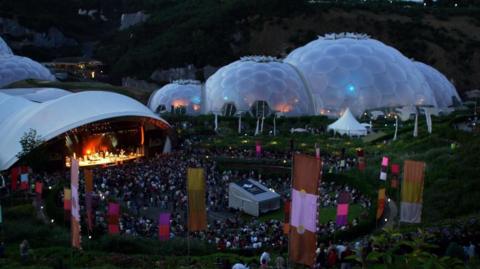 Crowds beginning to form around the stage in front of the Eden Project on a previous year, with the two, interconnected biomes in the background.