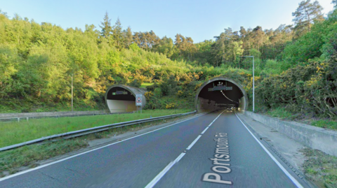 A stretch of road leading into a tunnel. It is a sunny day.