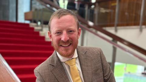 Newcastle City Council leader Colin Ferguson/ he is wearing a grey suit and yellow tie and has short brown hair and a short beard. He is standing on the stairwell inside Newcastle Civic Centre.