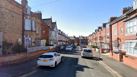 Google view of Clarence Avenue in Bridlington. There are houses on either side of the road and vehicles parked in bays along the street.