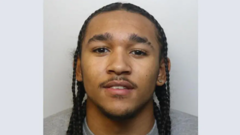 A police mugshot of Joel Binnings. He has long dreadlocks and is wearing a grey sweatshirt