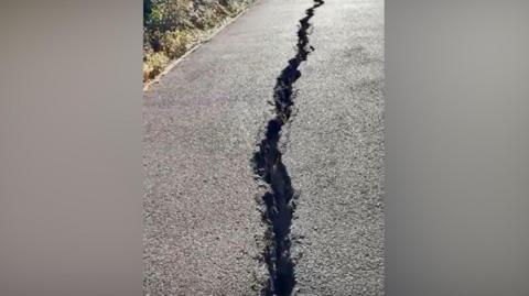 A close-up image of a long deep crack in a pavement