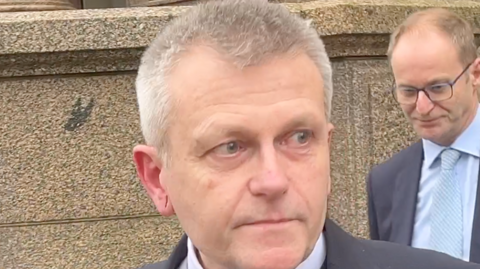 A man called Philip Ozouf outside Jersey's Royal Court building. Another man in a suit is stood behind him.