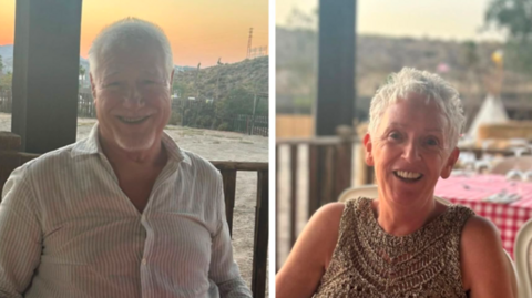 A smiling man and woman sat outside in the sun. 