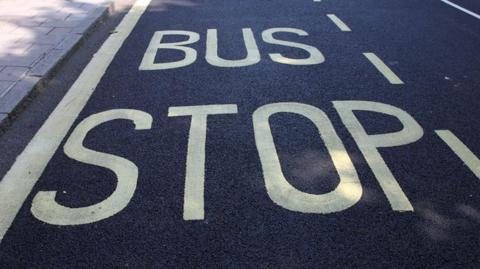 Generic image of a bus stop sign painted in yellow capitals against the black asphalt of a road
