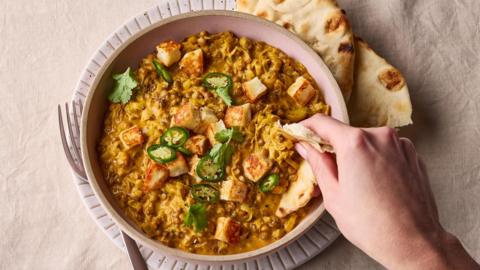 Creamy coconut lentil curry with crispy halloumi in a light pink bowl on a linen background. 