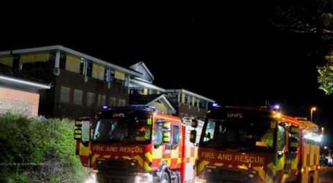 Two fire engines outside a large building with boarded up windows - it is night.