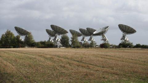 The Mullard Radio Astronomy Observatory, epicted by eight white satellite dishes with a field in front of it.